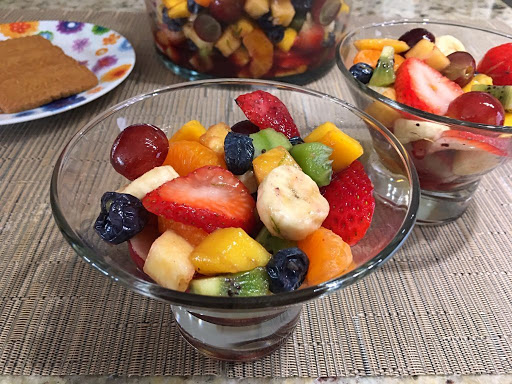 A couple bowls of fruit salad with a plate of cookies in the background.