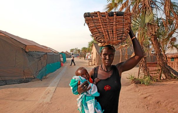 Nyandar Chuong carries her seven-month-old baby and a handmade crib she brought for the baby of her daughter, who was due to give birth at the MSF primary health-care facility in Leer.