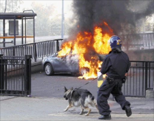 FIERY RETORT: A policeman and his dog walk towards a burning car in central Birmingham, England, after youths fought running battles with police. Photo: REUTERS