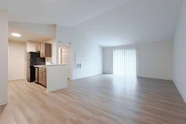 Open concept living room and kitchen with wood-style floors, vaulted ceiling, and a sliding glass door with vertical blinds