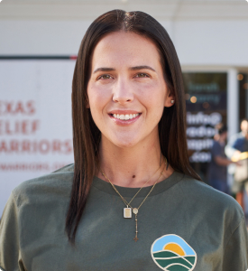 Cara in front of semi-trailer trucks being loaded with supplies by volunteers