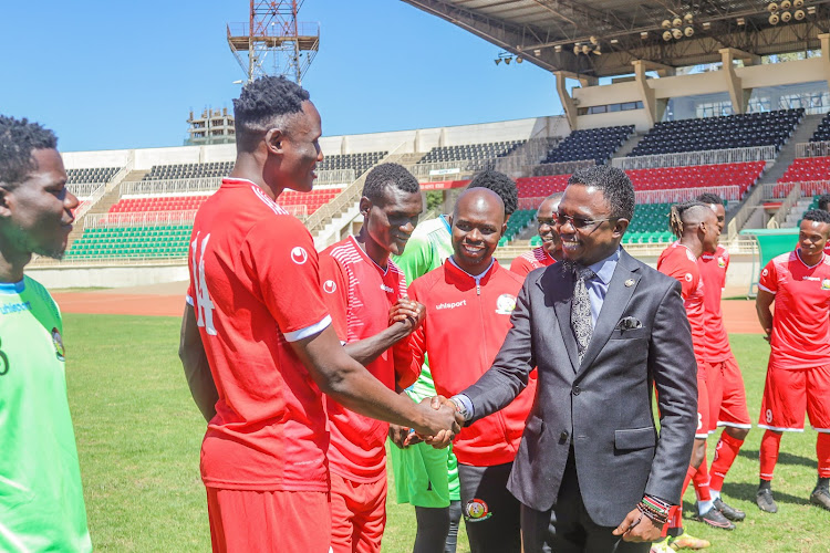 Sports CS Ababu Namwamba shakes hands with Harambee Stars skipper Michael Olunga during a visit to the team's training camp at Nyayo Stadium