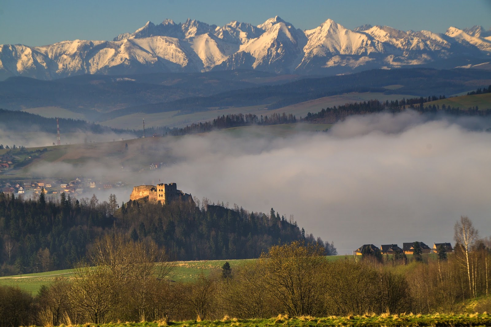 castle ruins in a cloudy forest with tall snow-covered tatry mountains in background during sunset in poland