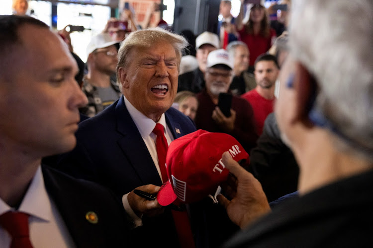 Former US President and Republican presidential candidate Donald Trump passes a signed hat as he rallies with supporters at a "commit to caucus" event at a Whiskey bar in Ankeny, Iowa, US December 2, 2023.