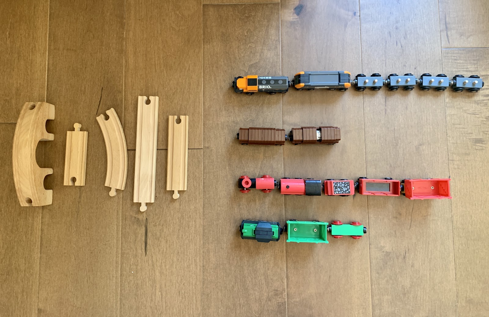 5 train track pieces. 3 are straight and 2 have curves. 4 rows of train cars. One row has 6 gray train cars. Then a row of 2 brown train cars. Next a row of 5 red train cars. And a row of 3 green train cars.