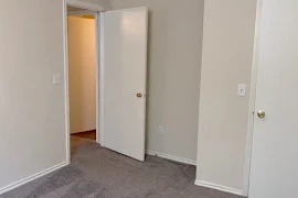 Interior view of an apartment showing an open door leading to another room with carpeted floors and white walls.