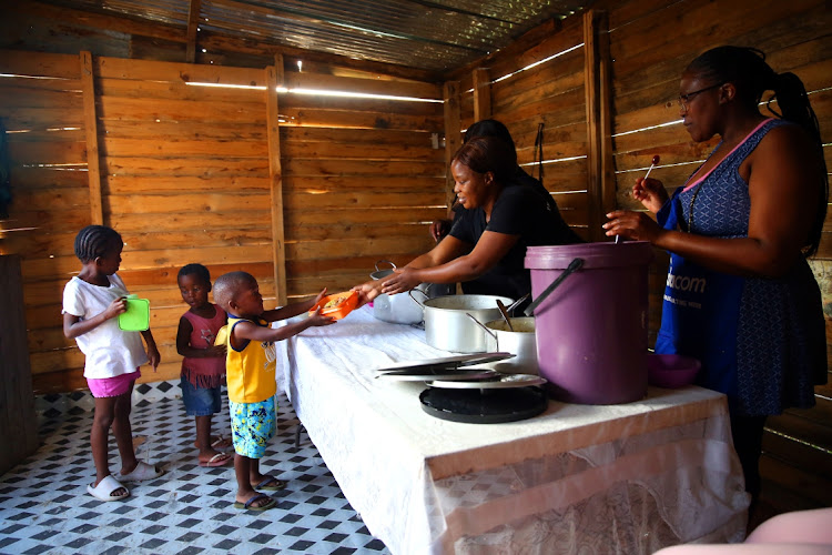 Pandora Ngantweni serves a hot meal to, from left, Ulunamda Shai, six, Ingakuwe Race, three, and Oyisa Ngantweni, three. Helping serve the food are Sanele Ncapayi, left, and Nojmpumelelo Race.