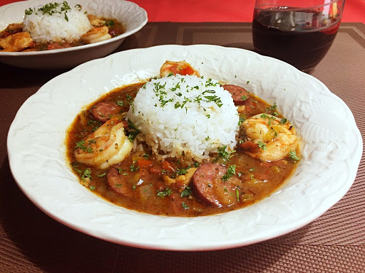 Meat and shrimp sitting in a broth with rice in the middle and some parsley sprinkled on top.