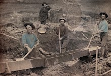 wassen van opgegraven grond: 3 ingekleurde mannen met een schop, een vierde achteraan kijkt toe