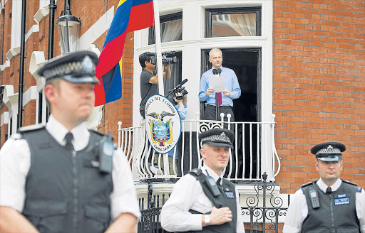 READY TO LEAVE: Wikileaks founder Julian Assange delivers a statement on the balcony inside the Ecuador Embassy, London, as police officers stand guard below. Assange says he will hand himself in to British police today if a UN panel probing sex assault charges rules against him Picture: EPA