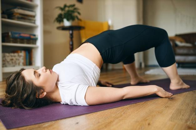 Beautiful plus size young woman practicing yoga, doing bridge pose, lying on mat with feet on floor, bending knees and pushing tailbone upward, stimulating abdominal organs, stretching spine and chest Free Photo