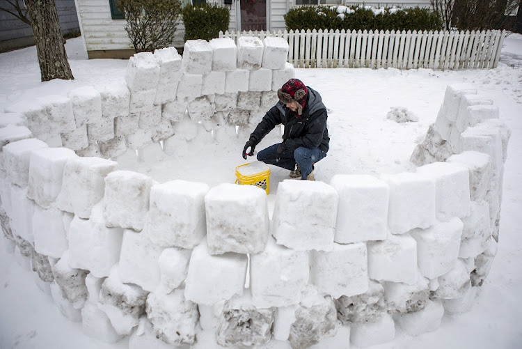 Jeremy Seidt, 44, packs snow that he shoveled off his driveway into an empty cat litter bucket as he works on making an igloo in the front yard of his Sharon Township home in Columbus, Ohio, US February 15, 2021.