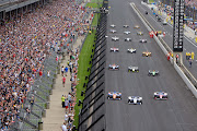 Fans look on as the cars drive three-wide down the front stretch on the pace laps before the start of the NTT IndyCar Series 103rd running of the Indianapolis 500 on May 26 2019, at the Indianapolis Motor Speedway in Indianapolis, Indiana.