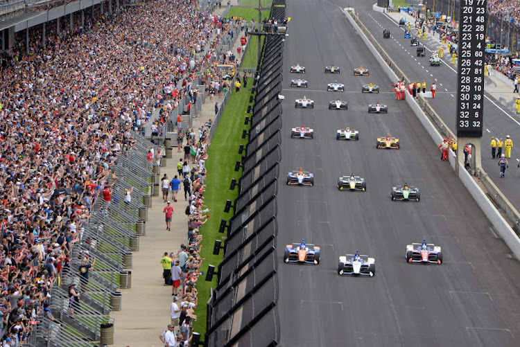 Fans look on as the cars drive three-wide down the front stretch on the pace laps before the start of the NTT IndyCar Series 103rd running of the Indianapolis 500 on May 26 2019, at the Indianapolis Motor Speedway in Indianapolis, Indiana.