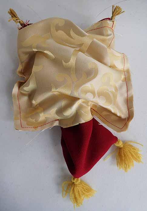 The red outer layer of the bag is pulled through the cream silk inner layer through the hole left at the opening. The ends of the cord are visible at the top, while two of the tassels are visible at the bottom.