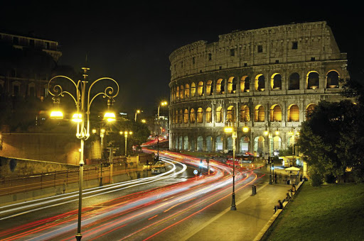 Traffic rushes by the Coliseum in Rome at night.