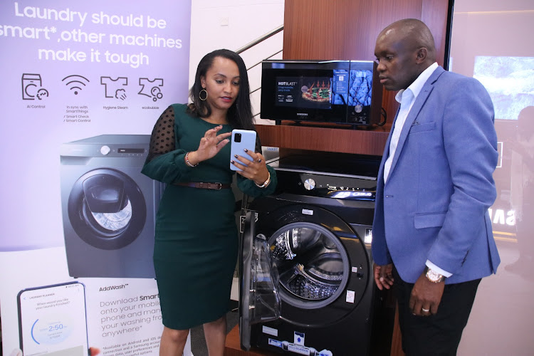 Samsung East Africa, Consumer Electronics Marketing Manager Irene Mwangi demonstrates to Head of Consumer Electronics Sam Odhiambo the use the AI feature on the Samsung washing machine.