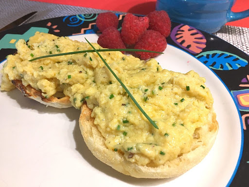 Scrambled eggs on English muffins garnished with chives and raspberries.