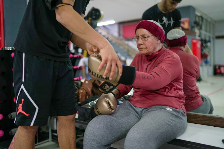 Trainer Muhammet Ali Kardas adjusts the gloves of Nancy Van Der Stracten, 75-year-old suffering from Parkinson's disease, before they start to practice boxing at a boxing club in the southern resort city of Antalya, Turkey, February 26, 2021.