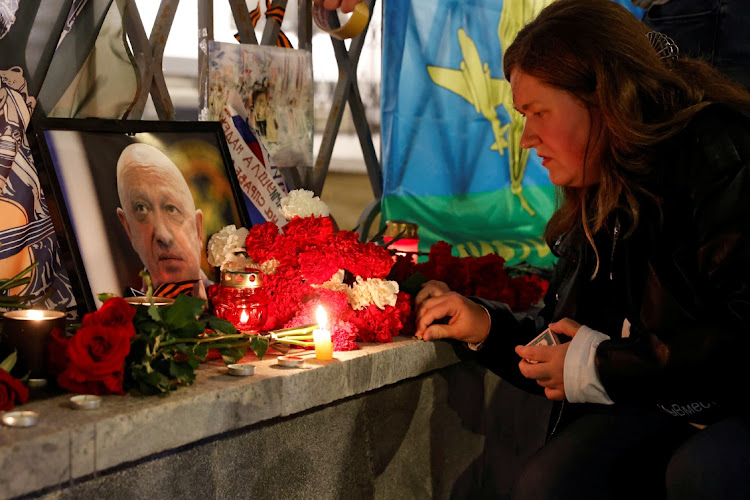 A woman lights a candle in front of a portrait of Wagner mercenary chief Yevgeny Prigozhin at a makeshift memorial in Moscow.