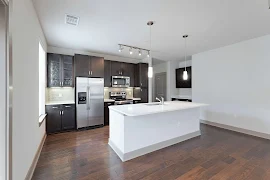 Kitchen with dark wood cabinets, white quartz countertops, white island with sink, stainless steel appliances, wood floors