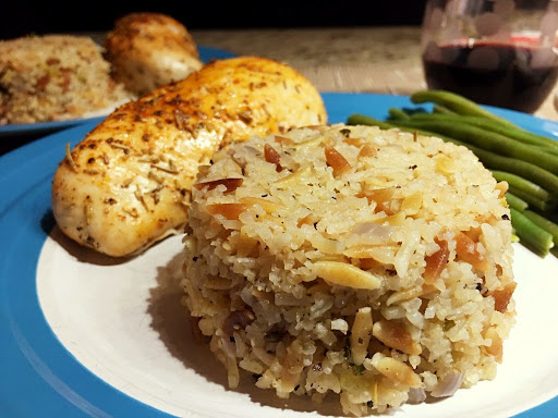 Rice on a blue/white plate along with a grilled chicken breast and some green beans.