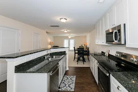 Kitchen with wood-inspired flooring, white cabinets, dark countertops, & stainless steel appliances. 