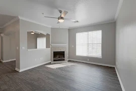 Living room with fireplace with mantel, double window with blinds, wood plank floors and arched pass-through window to dining